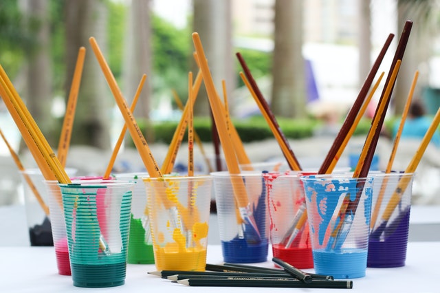 пластмасови чаши с различни цветове боя за рисуване и четки за рисуване