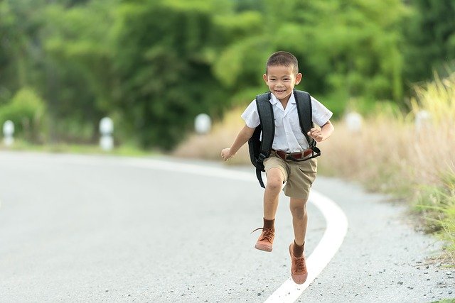 момче подскача от щастие по път за училище с раница за училище