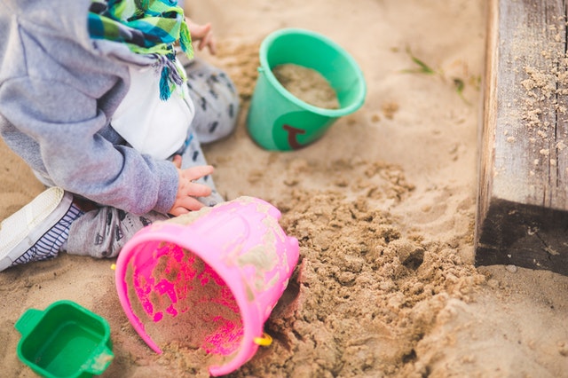 малко момченце играещо в пясъка с зелена и синя кофичка