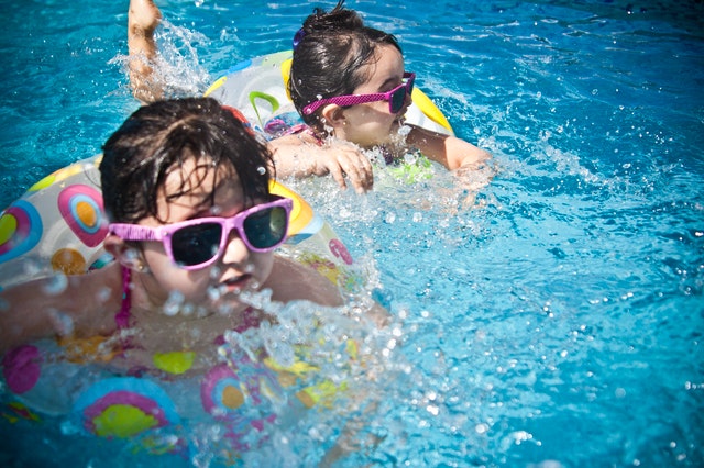две момиченца с очила плуват в басейн с пояси 