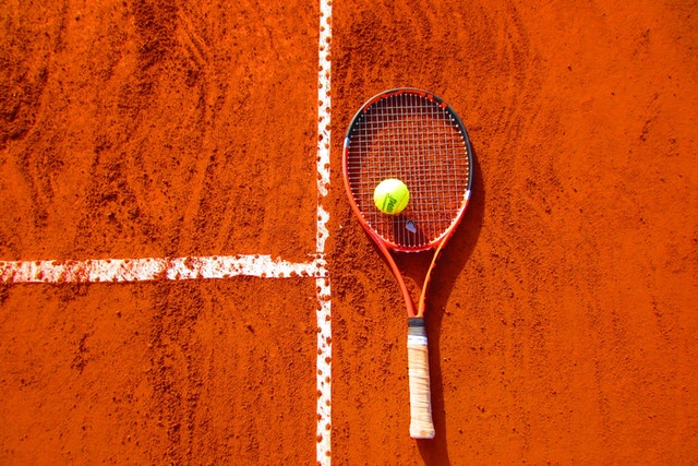 тенис ракета и тенис топка поставени върху червен корт